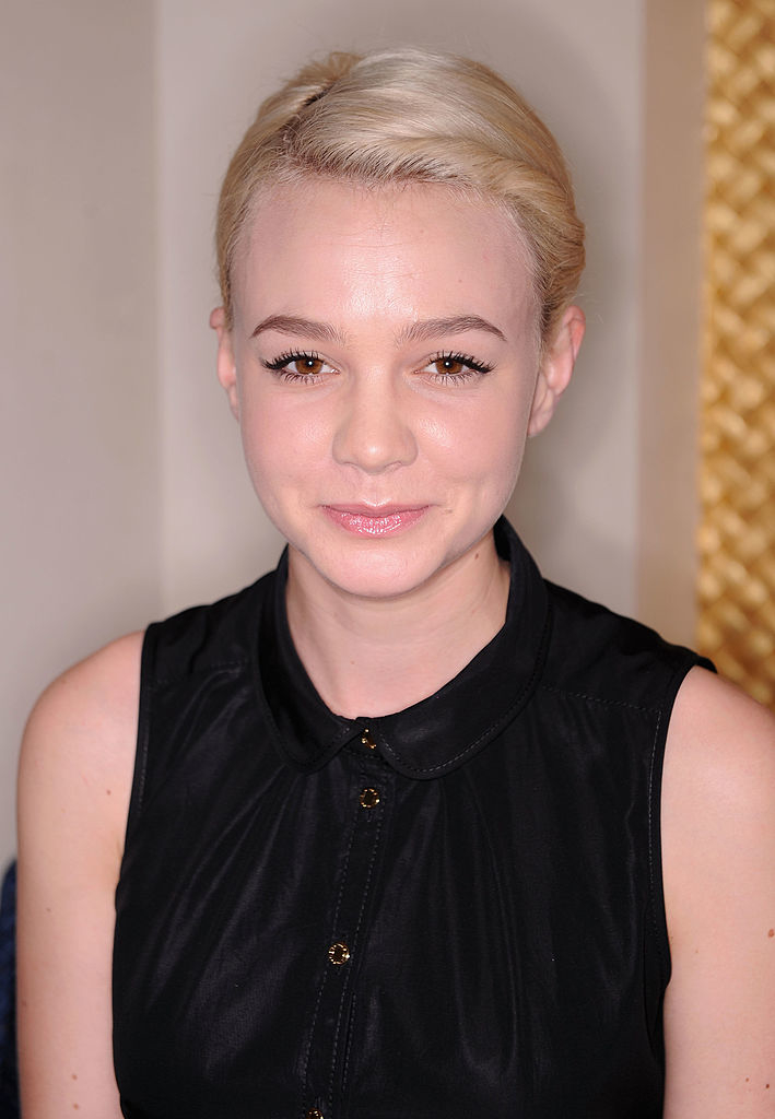 Carey Mulligan smiling, in a sleeveless collared blouse, with very short blonde hair