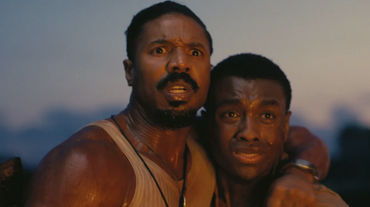 Michael B. Jordan holds another man close with a concerned expression in an emotional scene