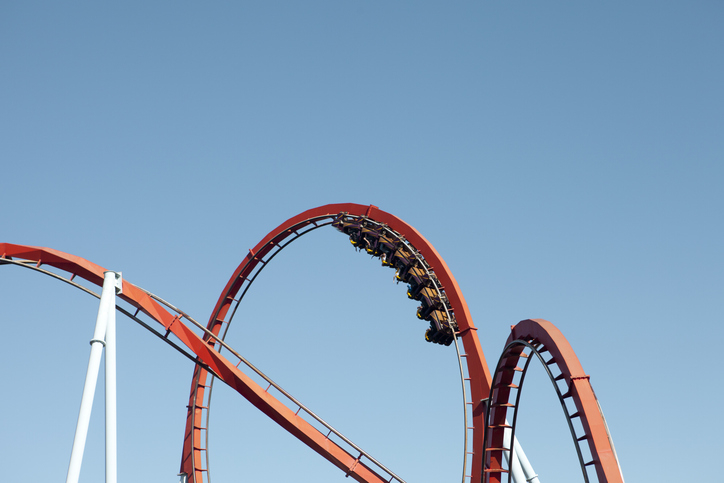A red roller coaster with riders is shown upside down in a loop against a clear blue sky