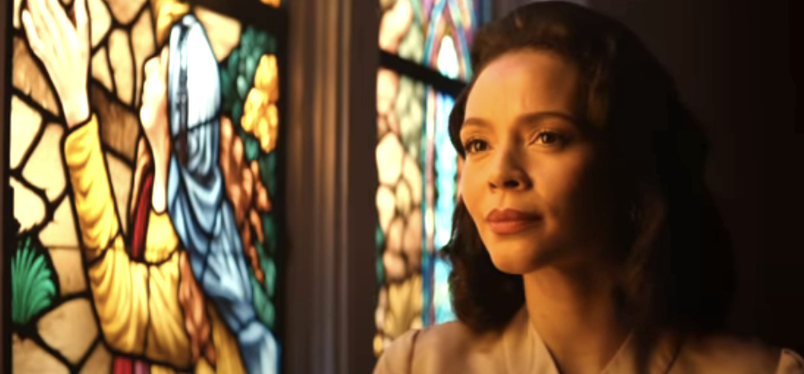 Angelina Johnson standing beside a stained-glass window featuring a colorful religious figure