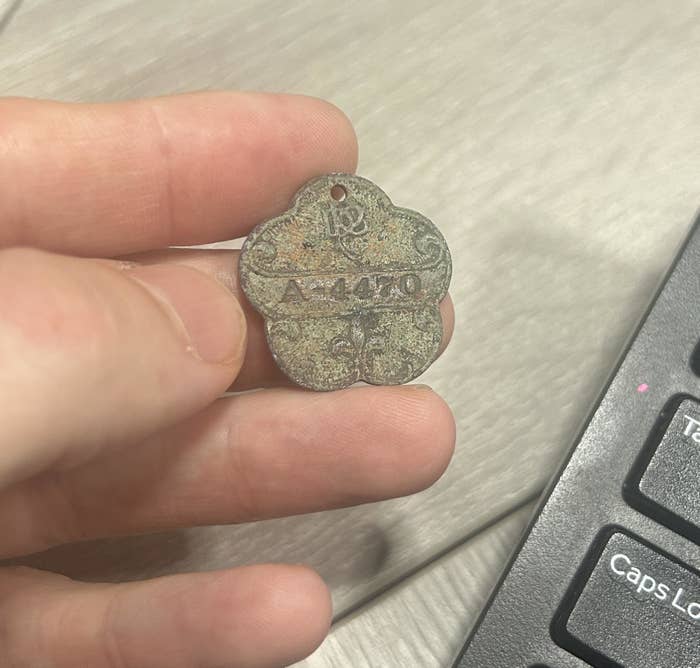Person holding an old, weathered metal tag with the inscription "A1440" next to a computer keyboard