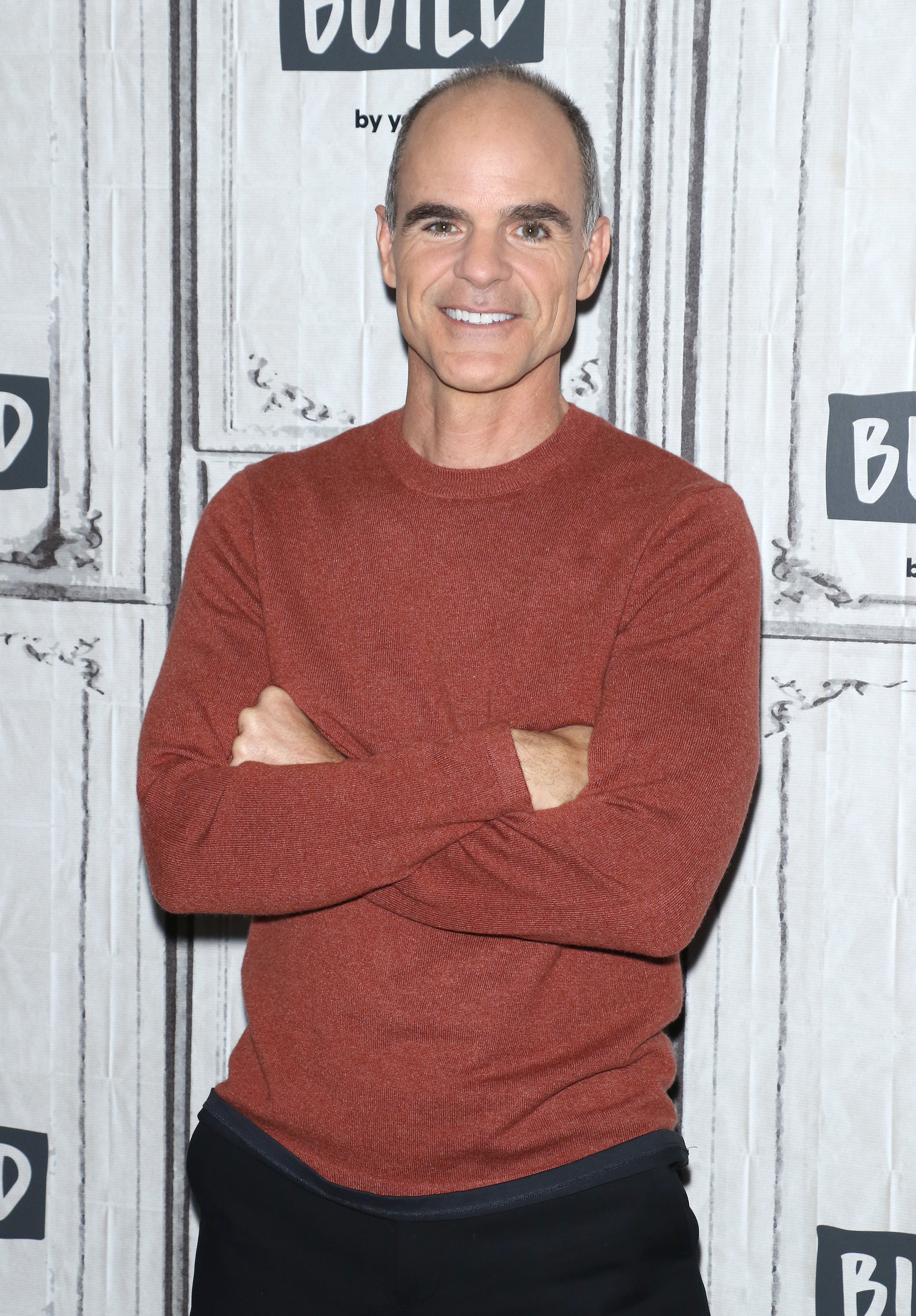 Michael Kelly stands with arms crossed in a long-sleeve shirt at a BUILD series event