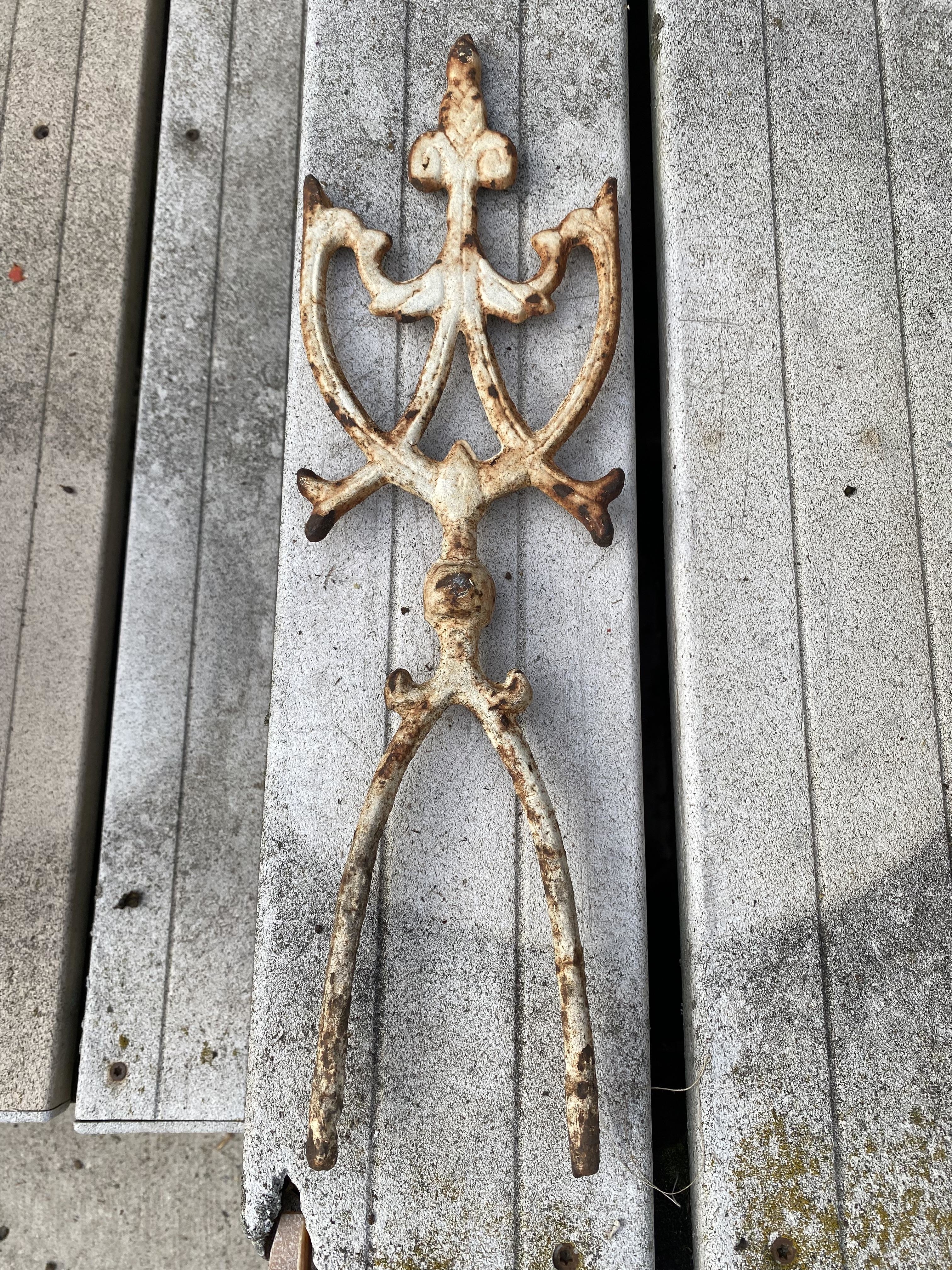Rusty, ornate metal tool with a complex handle and a pronged end, lying on a weathered wooden surface
