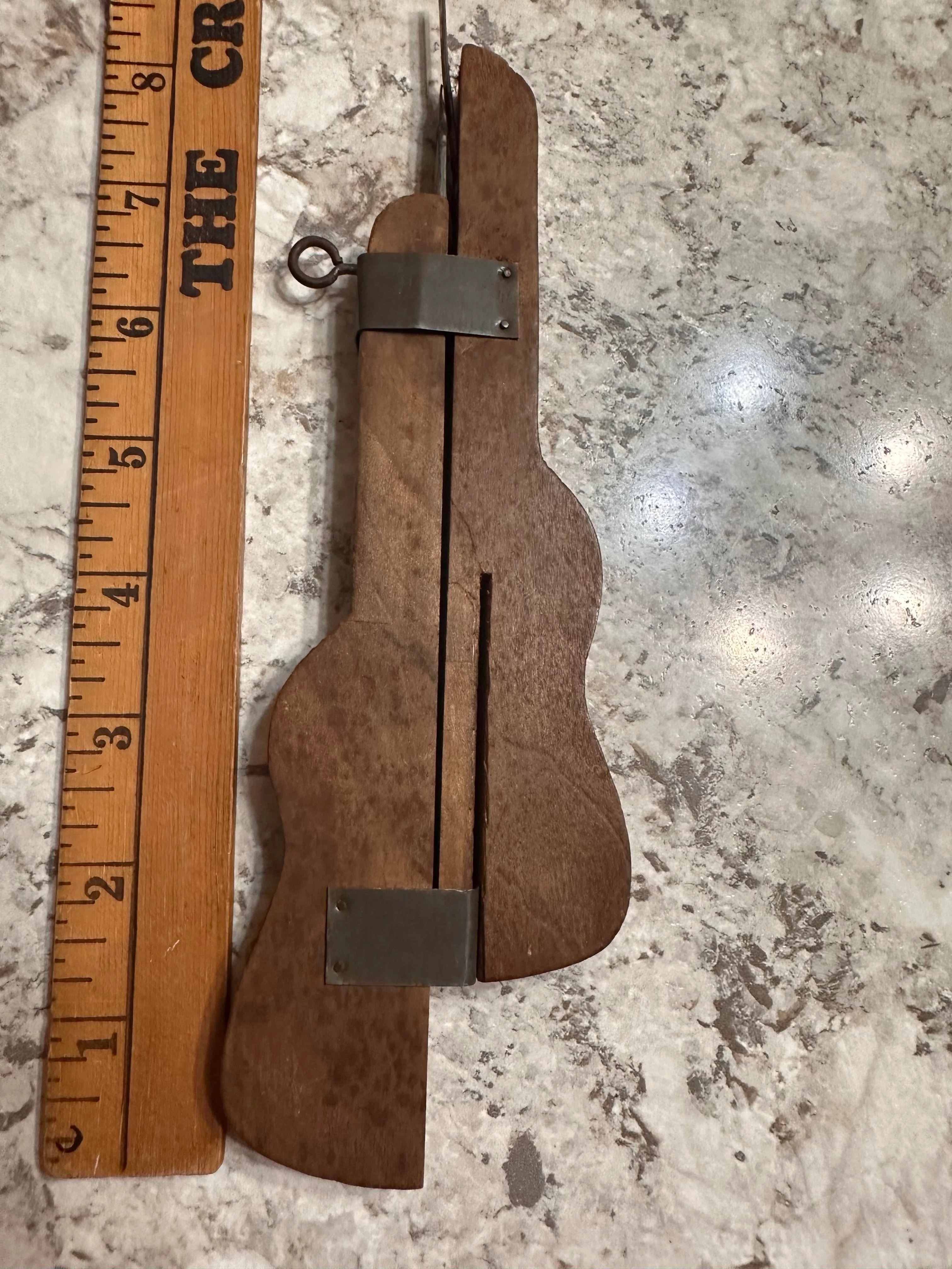 Wooden puzzle piece shaped like a guitar next to a ruler for scale. The puzzle has a metal clasp and hinge