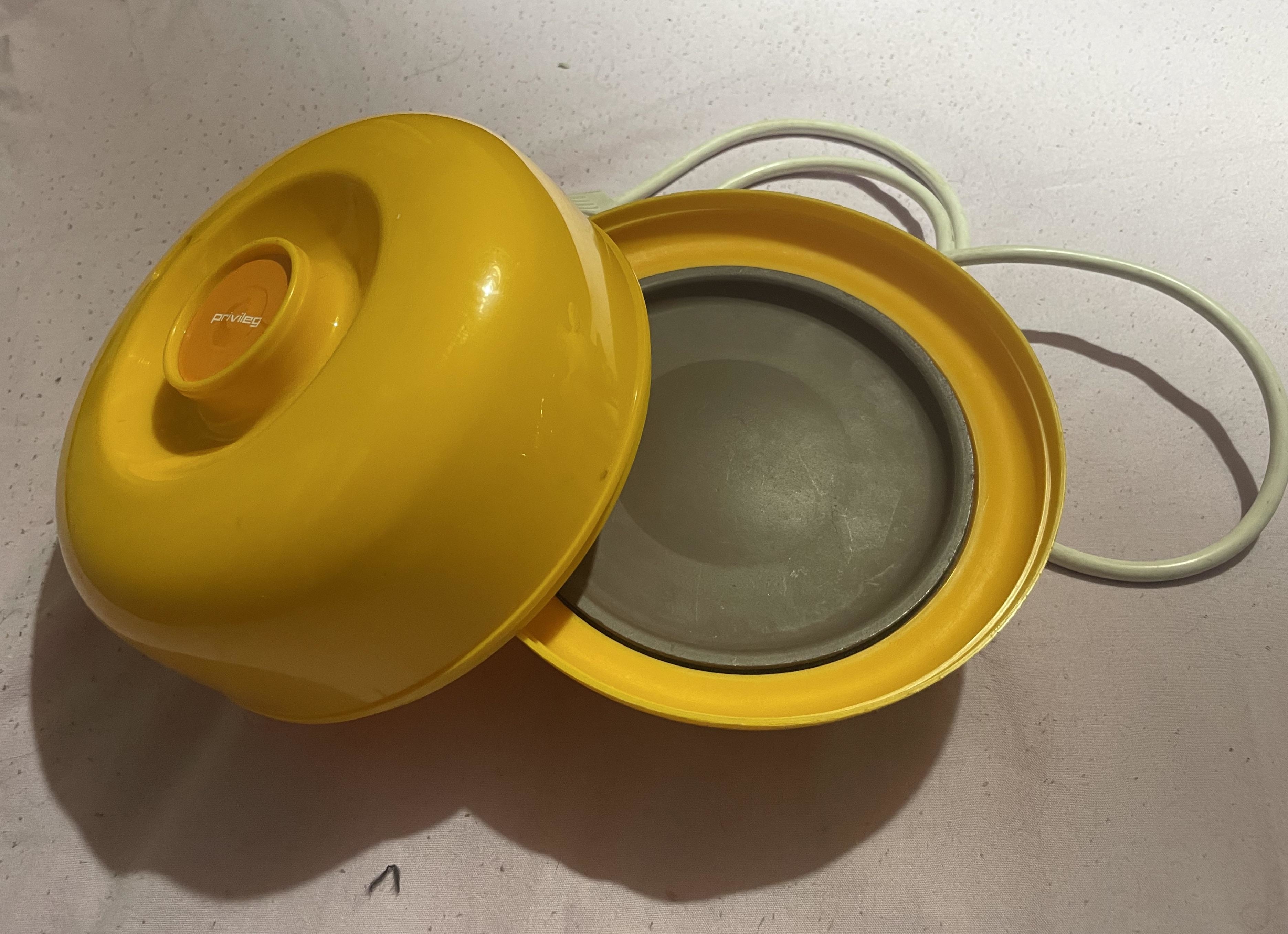 A vintage yellow egg cooker with an open lid revealing the cooking tray and electrical cord