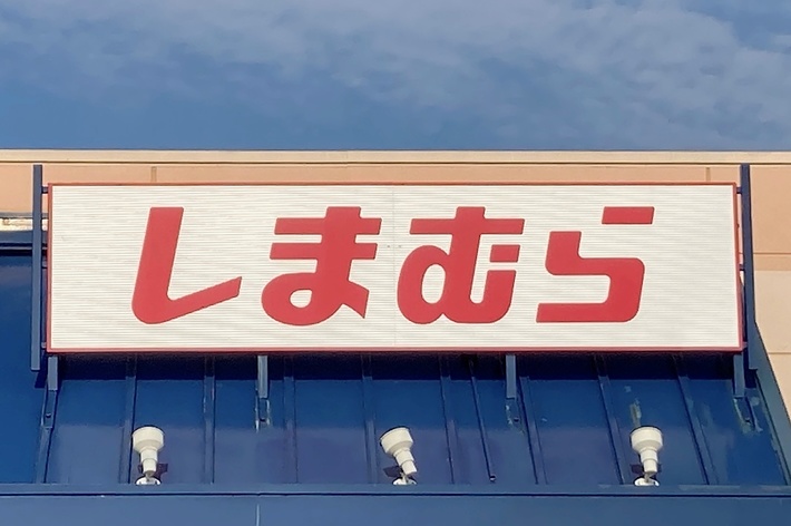 Sign in Japanese outside a storefront, reading &ldquo;しまむら,&rdquo; indicating the name of the store