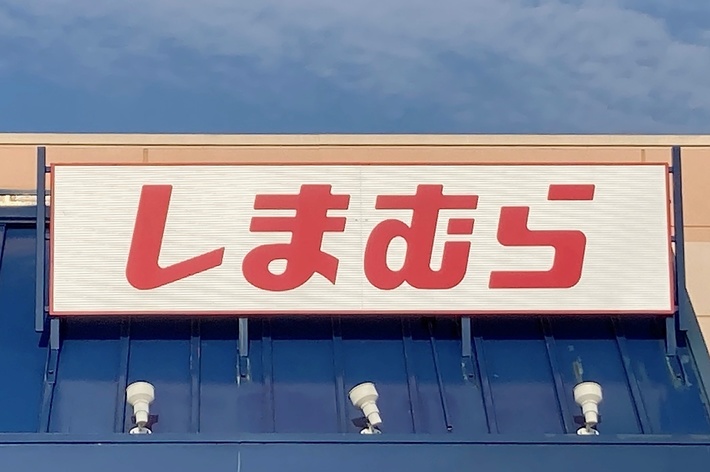 Storefront with Japanese text &ldquo;しまむら&rdquo; on a sign, located above glass windows and an accessible parking sign in front
