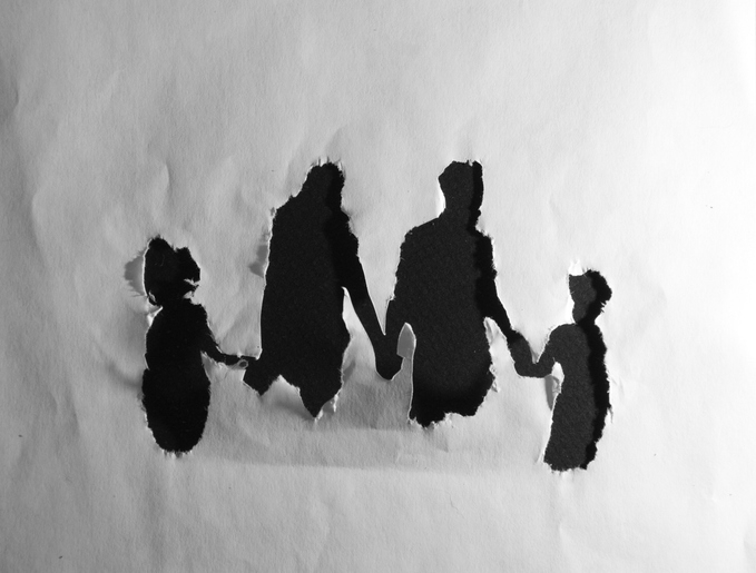 Silhouette of a family of four holding hands, created by tears in a piece of paper
