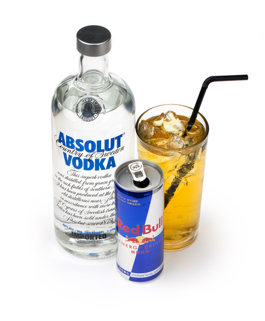 A bottle of Absolut vodka, a can of Red Bull energy drink, and a glass with a mixed drink and ice, with a straw
