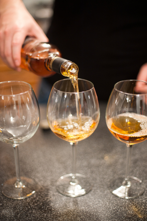 Close-up of a hand pouring white wine into one of three wine glasses on a countertop