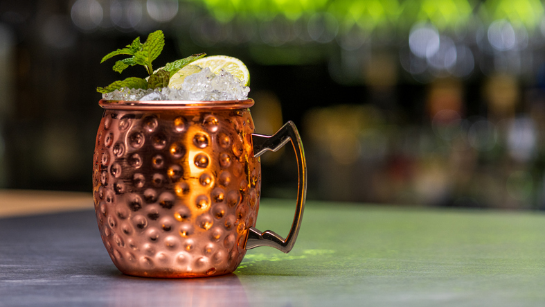 A copper mug filled with ice, topped with a lime wedge and a sprig of mint, sitting on a bar counter