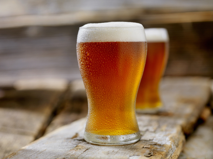 Close-up of two frosty beer glasses filled with amber beer, sitting on a rustic wooden surface