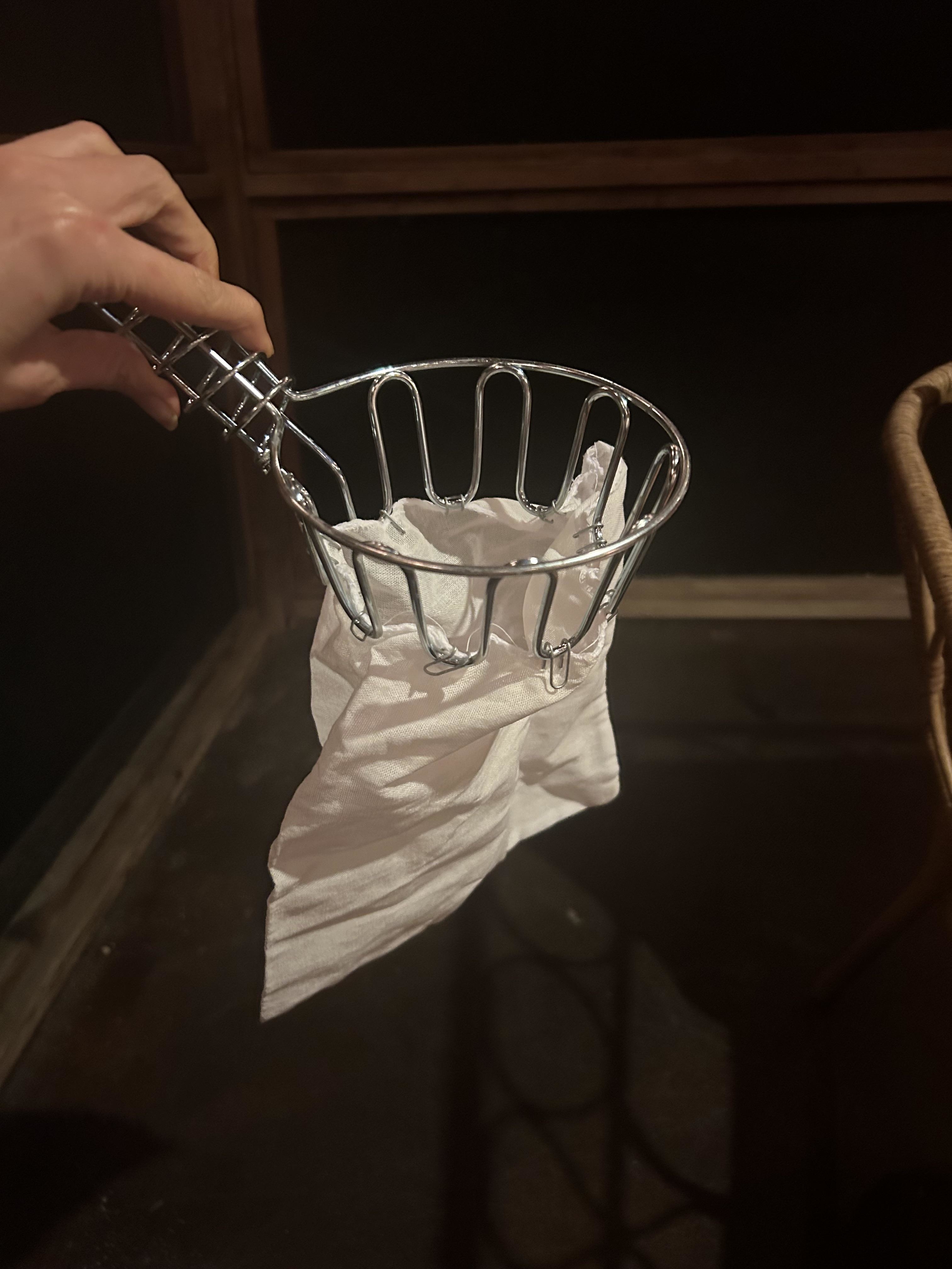 A hand is shown holding a metal basket-style small trash picker with a napkin caught in it. There are no people visible in the background