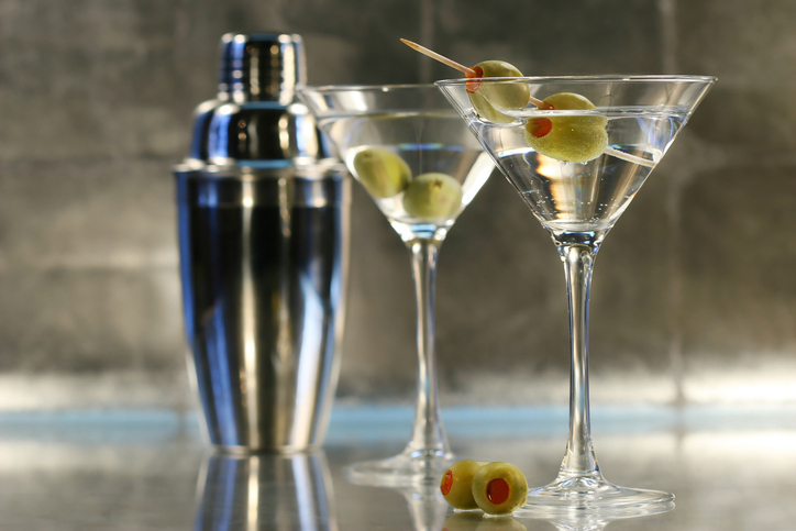 Two martini glasses with olives and a cocktail shaker in the background