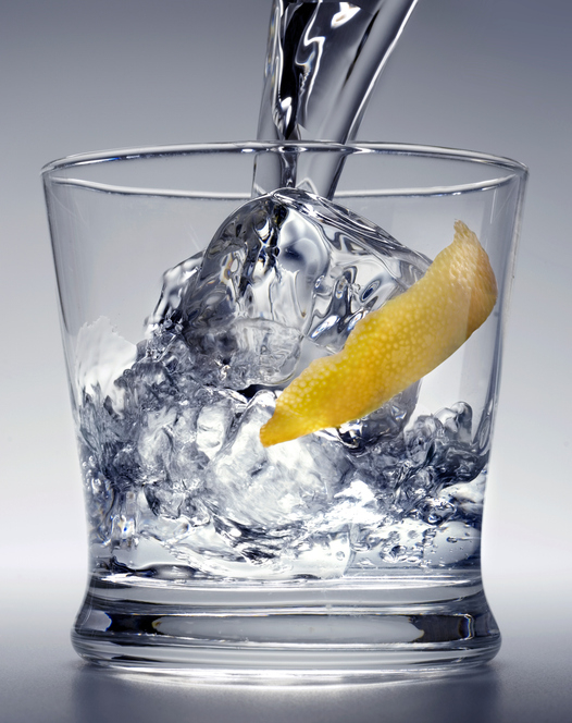 A glass filled with ice and a lemon peel is being filled with liquid