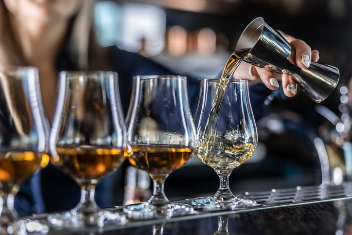 Bartender pouring whiskey into a glass, with several filled whiskey glasses lined up on a bar counter