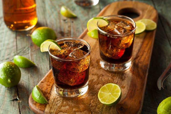 Two glasses of rum and cola with ice and lime wedges on a wooden board surrounded by fresh lime pieces