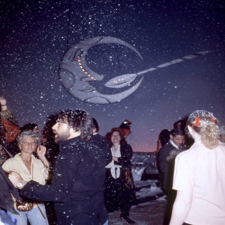 People dancing at a party themed with a moon and comet decoration. Snow-like effects are falling. No identifiable celebrities are in the image