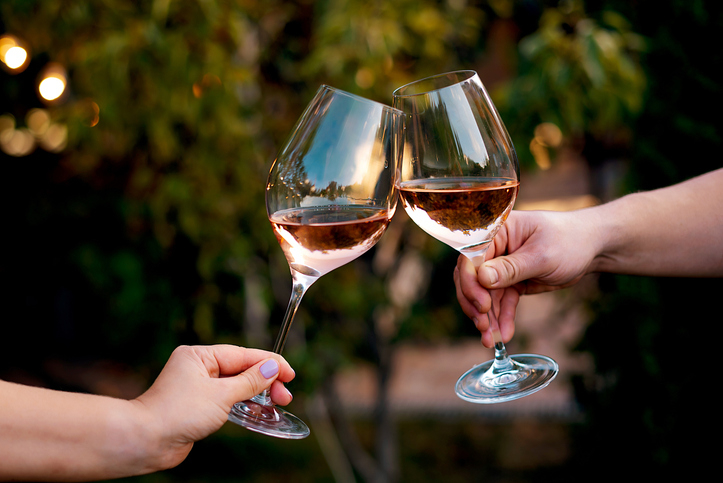 Two people clinking wine glasses in a toast outdoors, each holding a glass of rosé wine