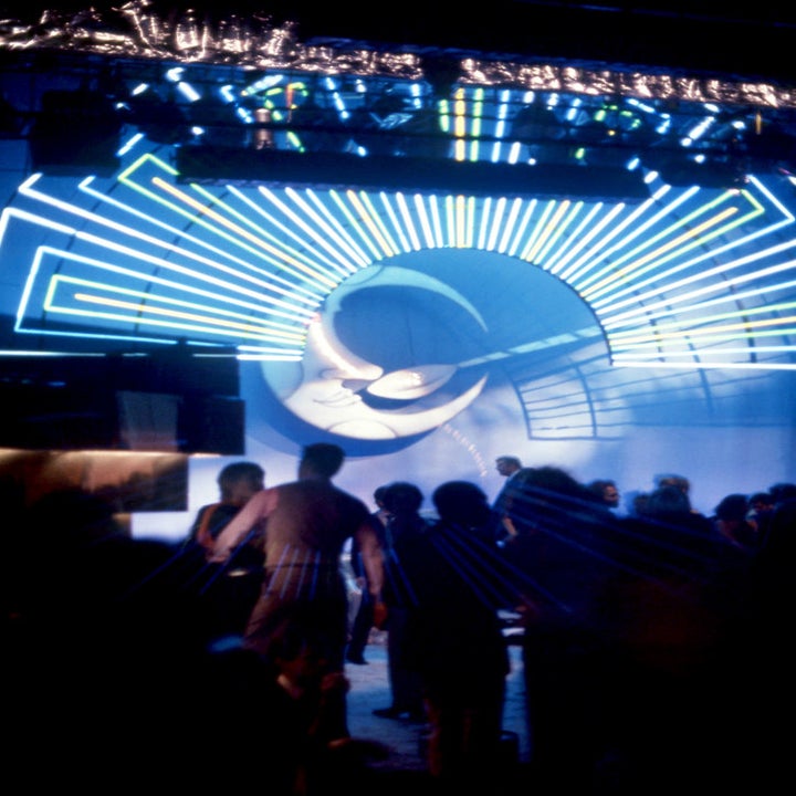 People dancing at a nightclub with a large illuminated DJ graphic and neon lights in the background