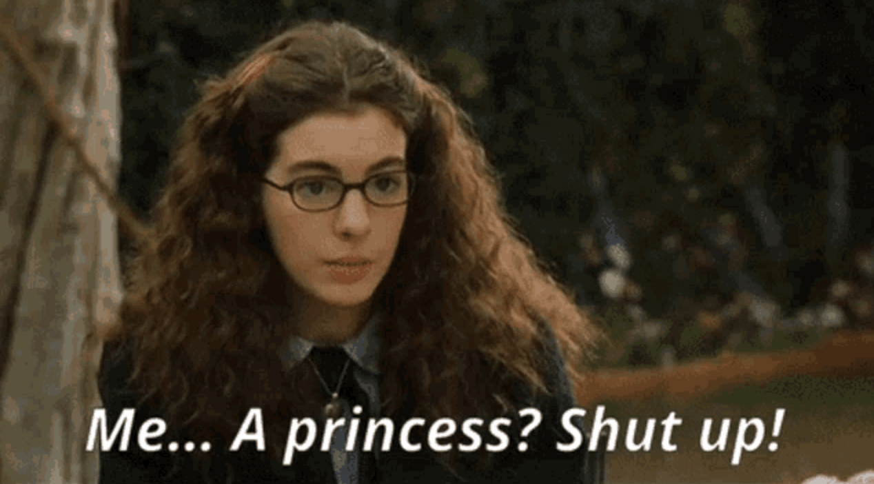 Anne Hathaway, in "The Princess Diaries," with curly hair and glasses, reacts with surprise, saying, "Me… A princess? Shut up!"