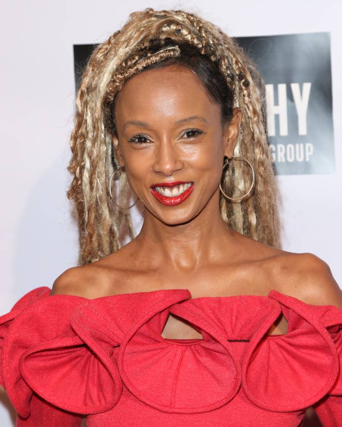 Trina McGee posing on the red carpet in an off-the-shoulder dress with ruffled details, wearing hoop earrings