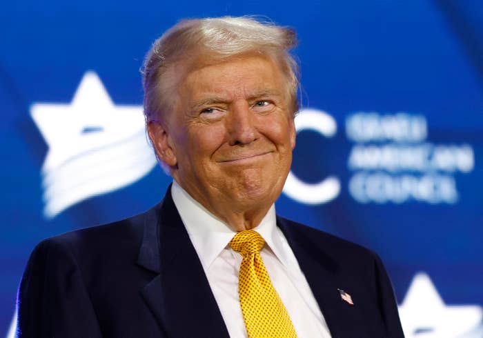 Donald Trump in a suit with a tie at an event with an Israeli-American Council logo in the background