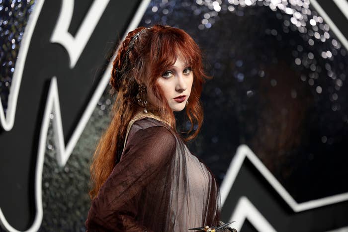 Chappell Roan in a medieval-themed outfit poses in front of a textured background with large geometric shapes