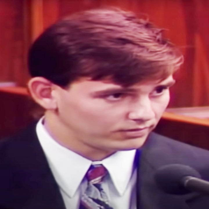 The real Andy Cano on witness stand in a courtroom, wearing a dark suit and tie, speaking into a microphone