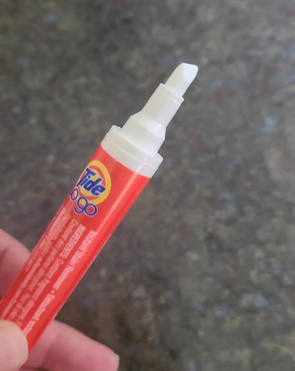 Hand holding a Tide To Go stain remover pen with a visible felt tip, angled for easy application