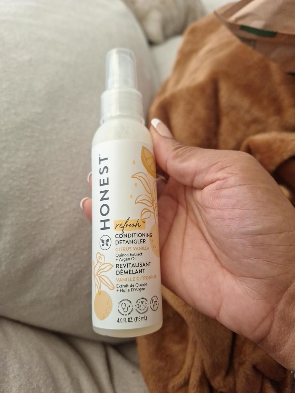 Hand holding a bottle of Honest conditioning detangler with citrus vanilla scent. Text on the bottle highlights the product's features and ingredients