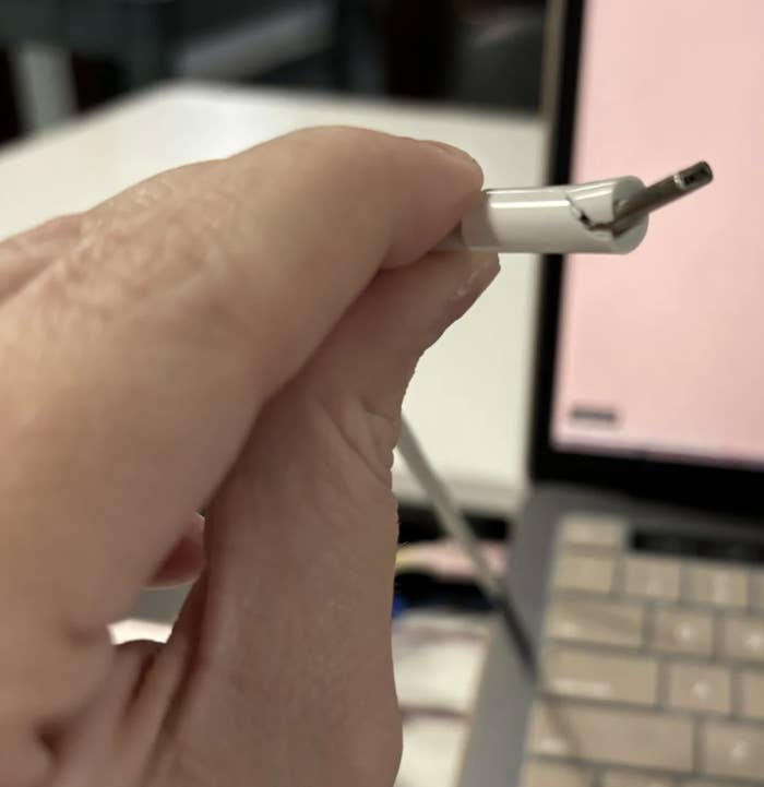Close-up of a hand holding a damaged USB cable in front of an open laptop