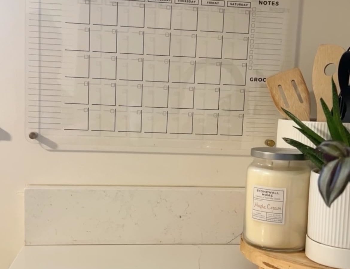 Clear acrylic family calendar mounted on a kitchen wall with the name "Andrade - Adams Family" at the top and organized into months, a to-do list, notes, and grocery sections