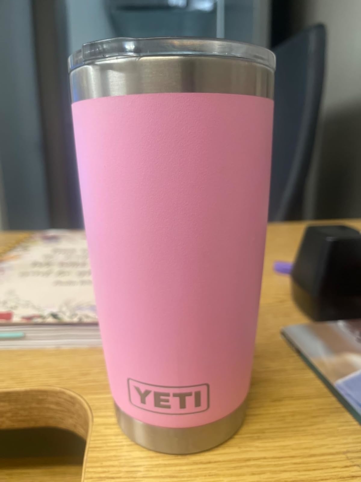 YETI pink insulated tumbler on a wooden desk with surrounding items like a book, a purple pen, and a stack of papers