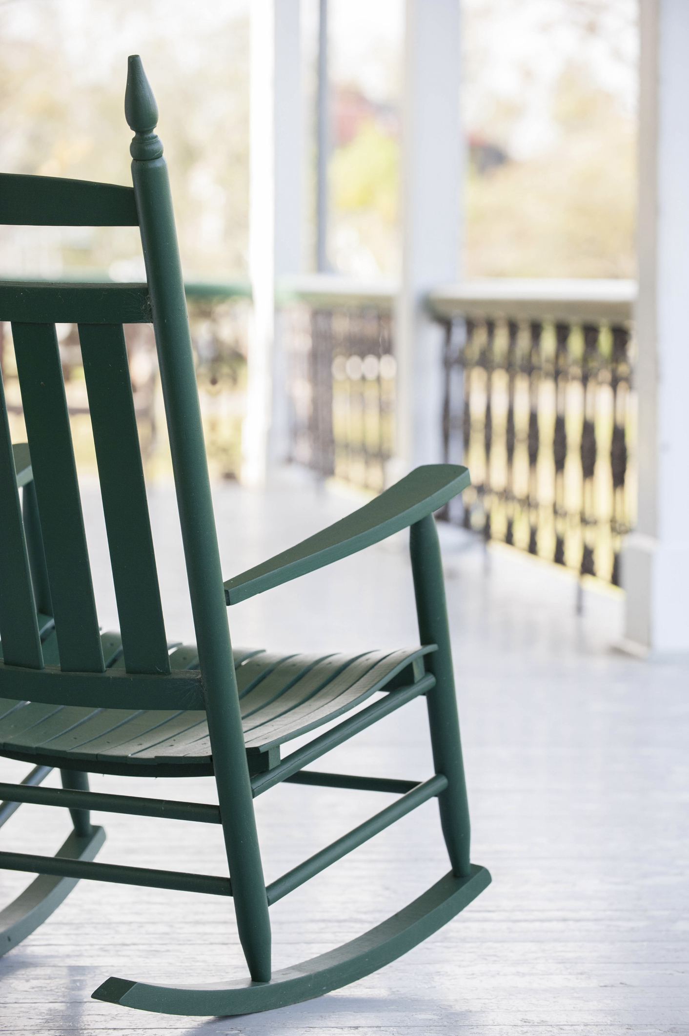 A green rocking chair sits on a porch overlooking a serene outdoor view. No people are present