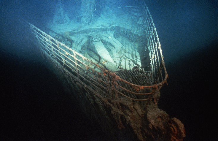 Underwater photograph of the Titanic wreck's bow, covered in rust and marine growth, resting on the ocean floor