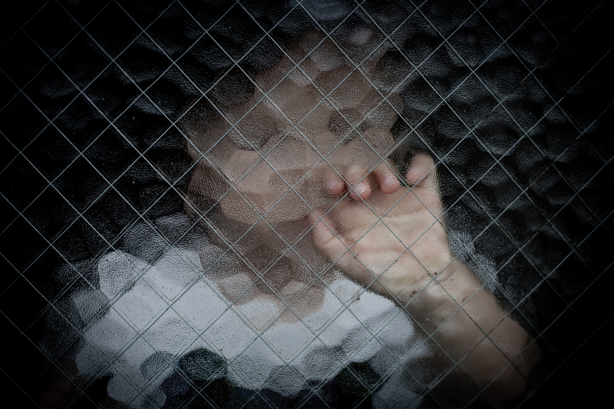 A child is seen behind a blurred, mesh-patterned glass panel, with their hand touching the glass