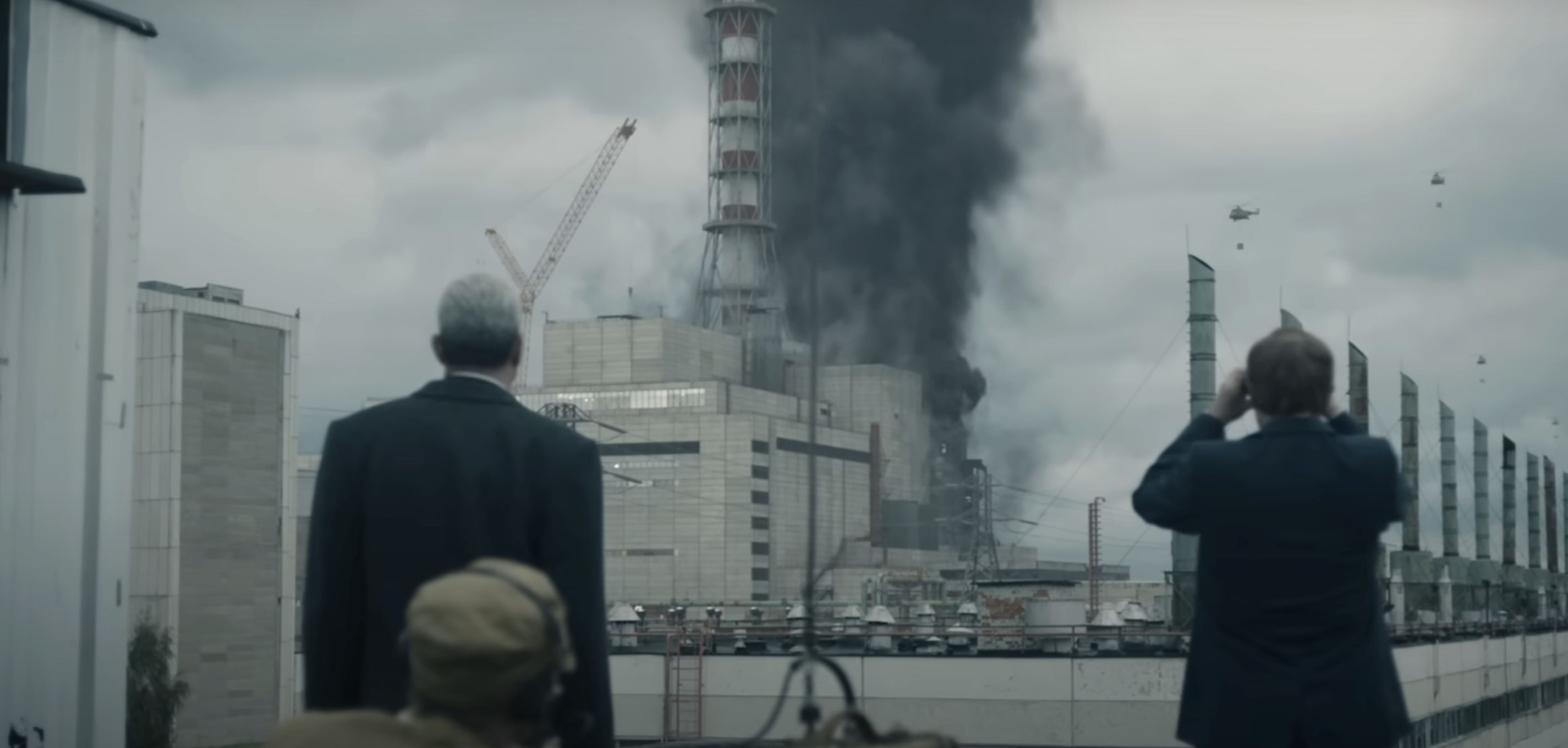 Scene from the TV series "Chernobyl" showing characters in business attire observing the smoking aftermath of the nuclear disaster