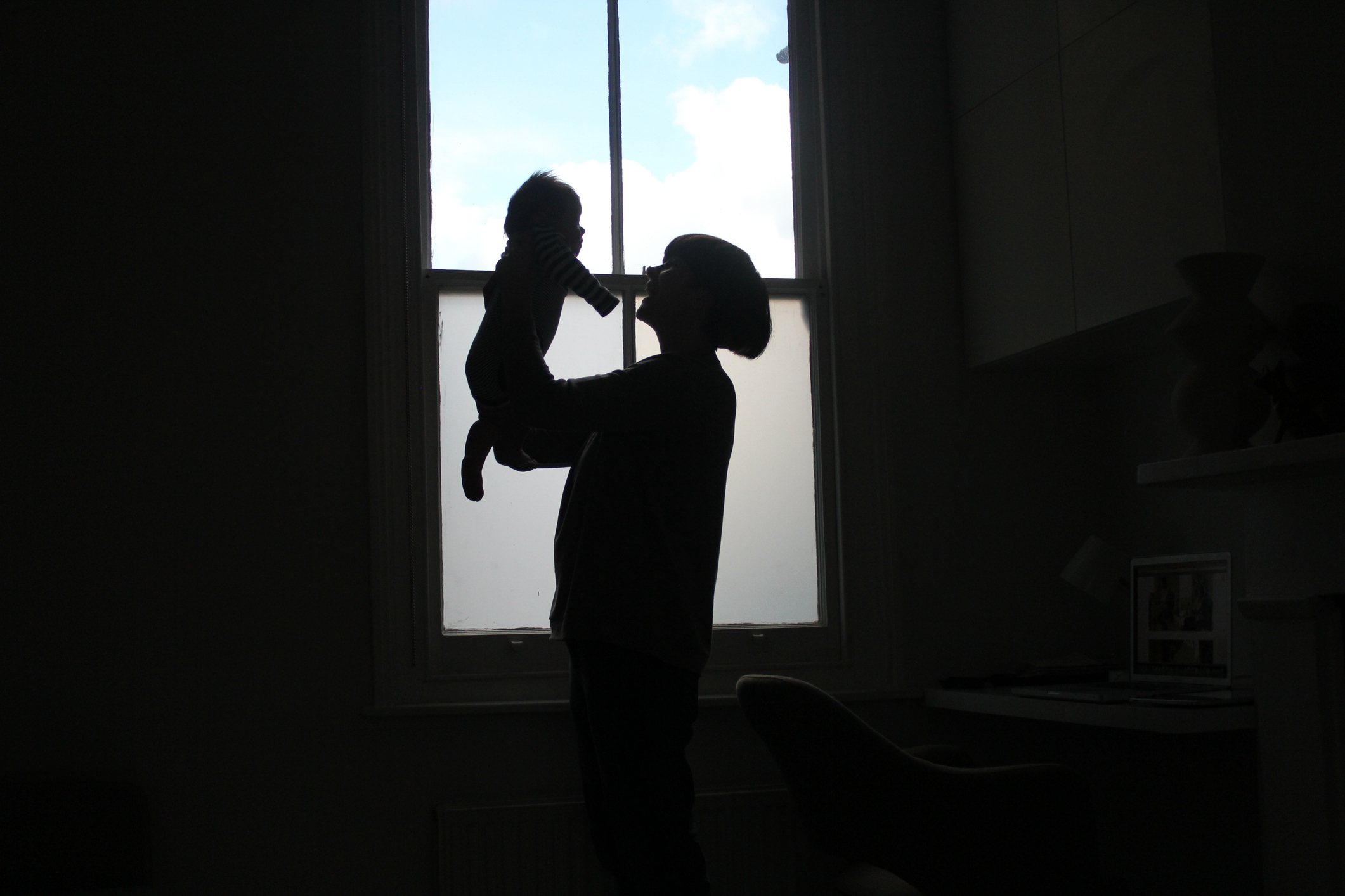 Silhouette of an adult lifting a child near a window, creating a heartwarming and playful moment