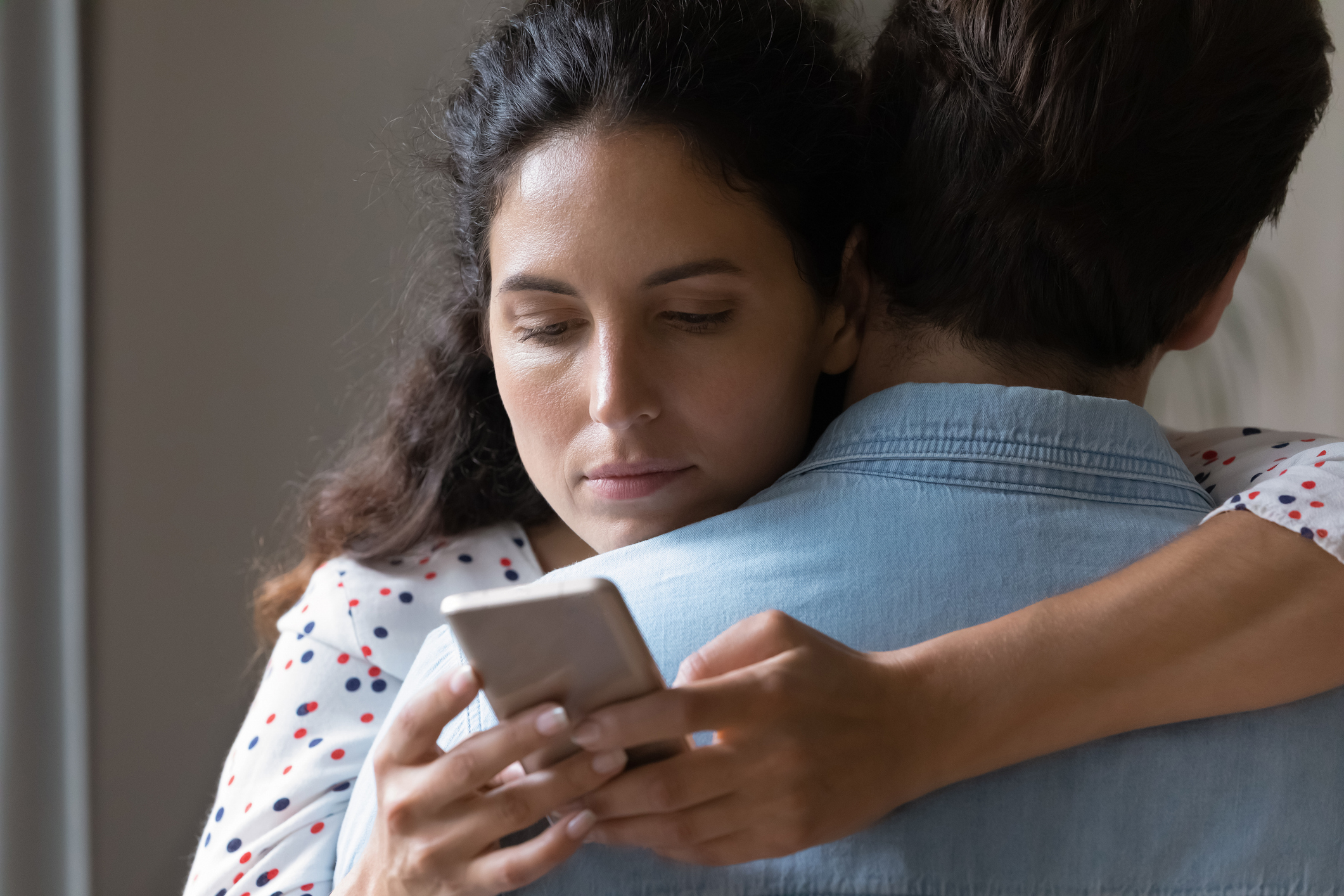 A woman, not named, looks concerned while hugging a man, also not named, and checking her phone