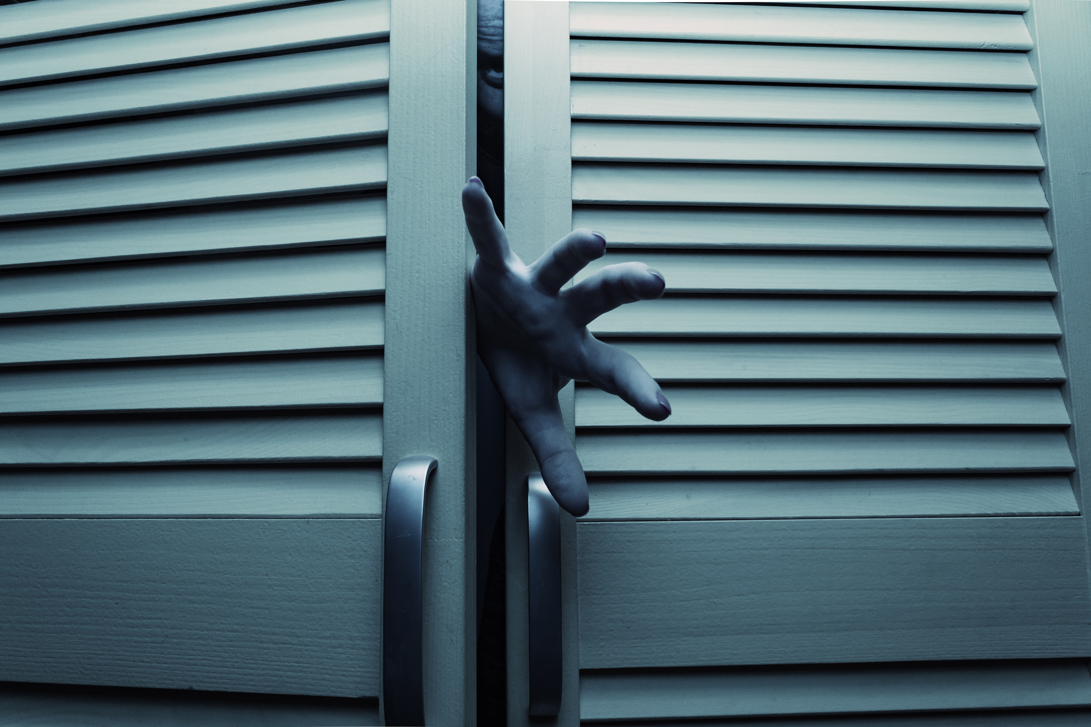 A hand is reaching out from behind slightly open louvered closet doors, creating a mysterious and eerie atmosphere