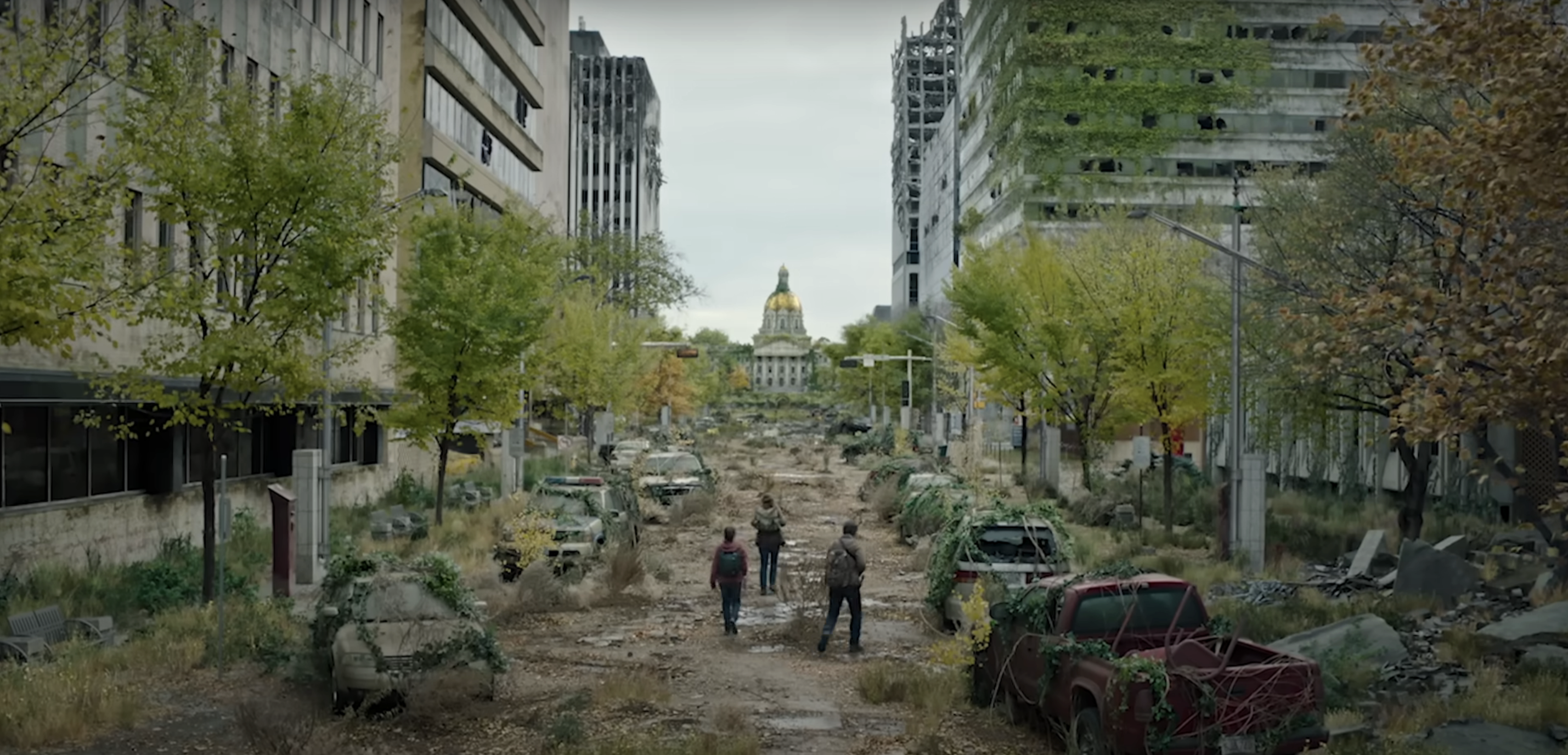 A post-apocalyptic city street with overgrown vegetation, abandoned cars, dilapidated buildings, and two people walking towards a distant dome-shaped building