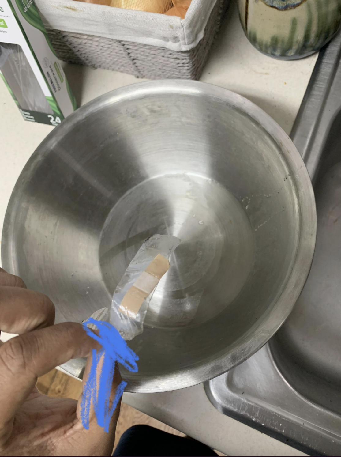 Hand pulling a used Band-Aid out of a metal mixing bowl over a kitchen sink