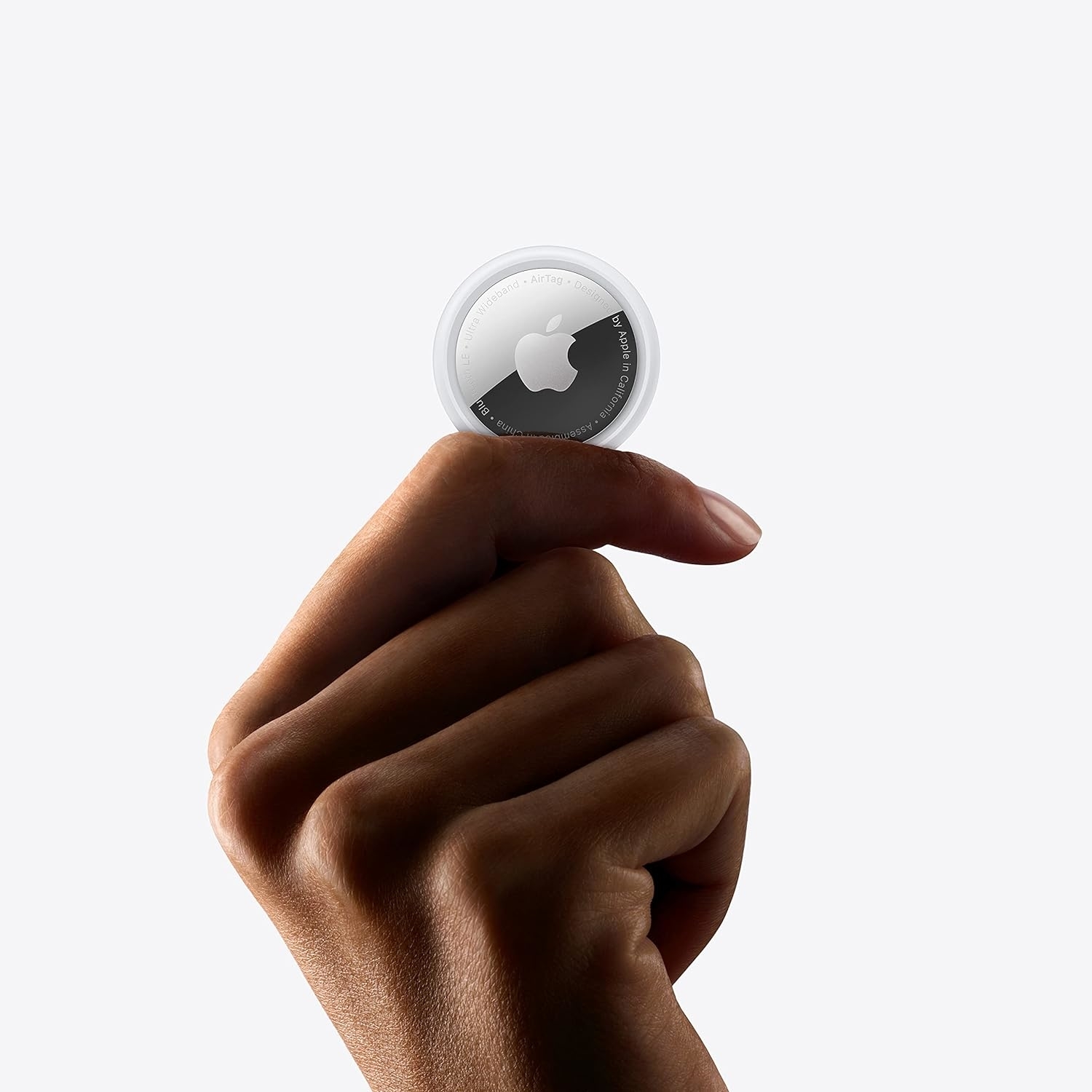 Hand holding an Apple AirTag, a small, round device used for tracking items