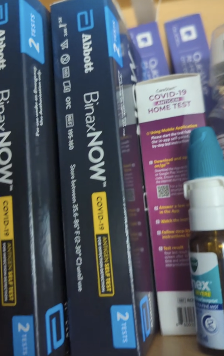 COVID-19 home test kits and a nasal spray on a store shelf. The brands shown are Abbott BinaxNOW and iHealth