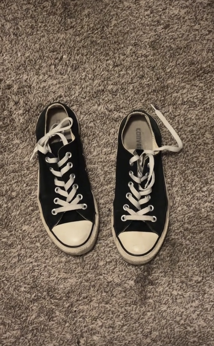 A pair of black Converse All Star sneakers with white laces and rubber toe caps placed on a textured carpet