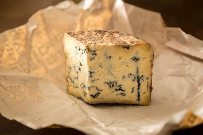 A piece of blue cheese sits on parchment paper, showing its creamy interior and blue mold veins