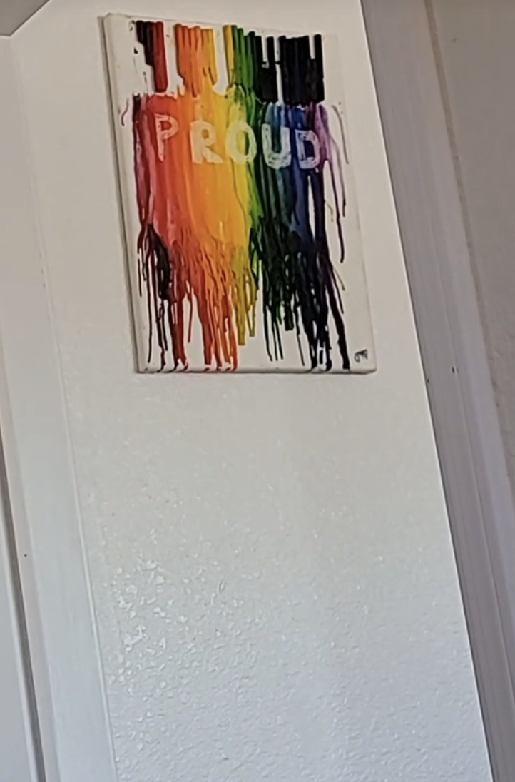 Wall art showing melted, colorful crayons forming a rainbow with the word "PROUD" in white letters