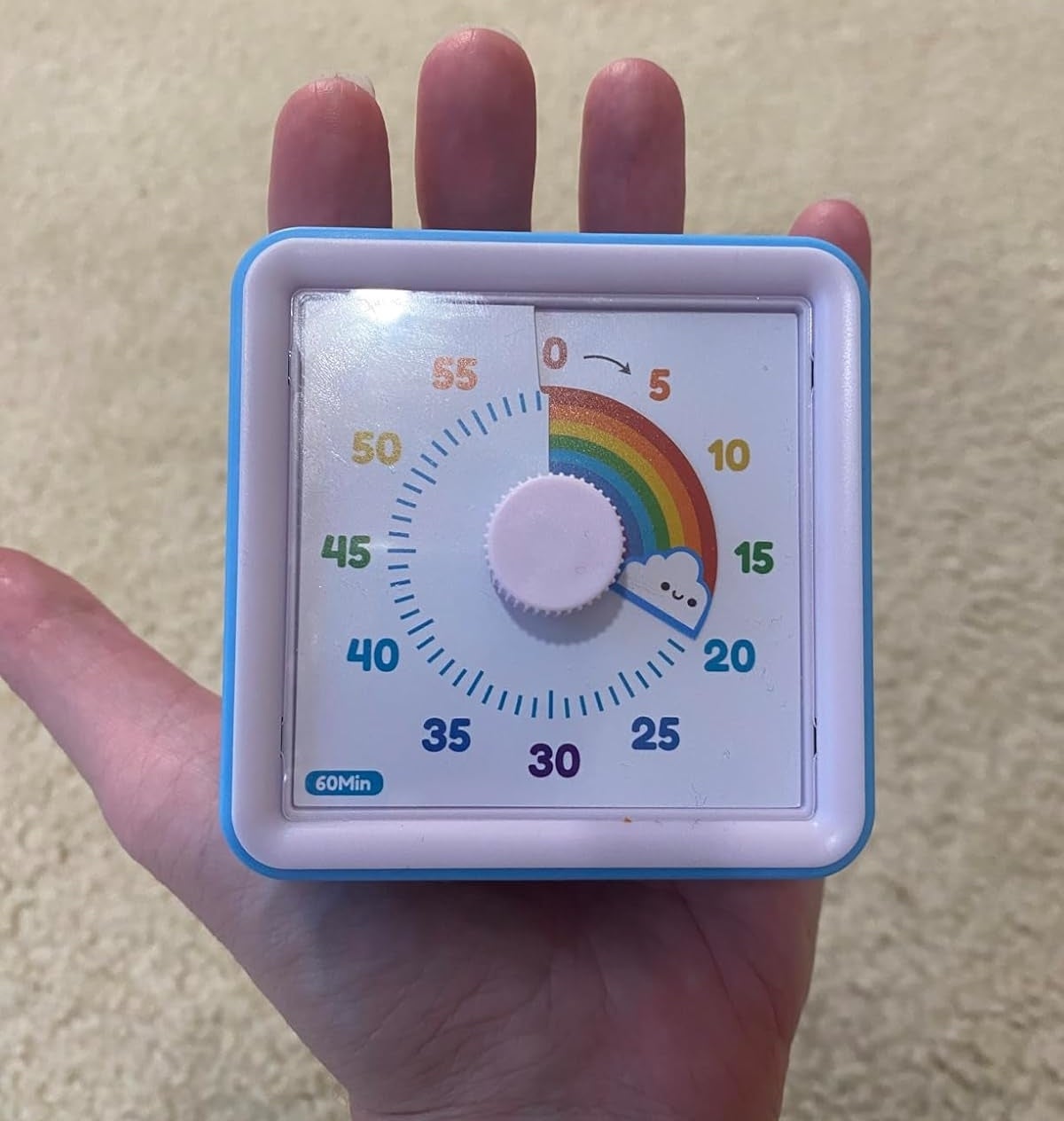 Person holding a square timer with rainbow and cloud design on the face, indicating time settings from 0 to 60 minutes