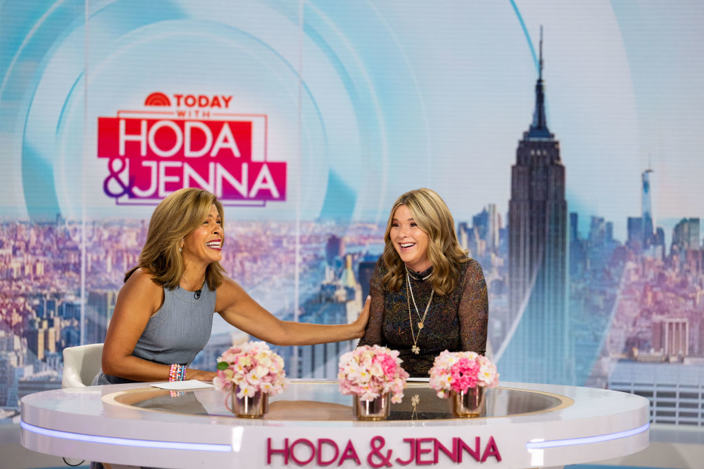 Hoda Kotb and Jenna Bush Hager laugh together on the "Today with Hoda &amp;amp; Jenna" set. Hoda wears a sleeveless dress, Jenna wears a lace-patterned long sleeve dress
